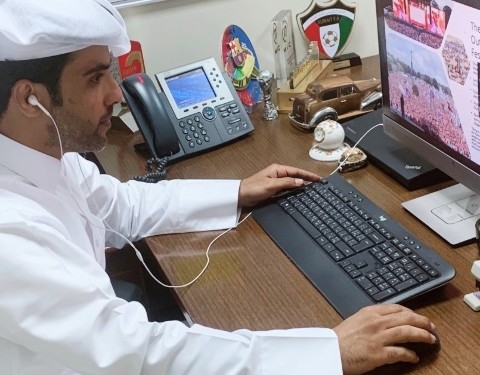 A man in traditional clothing uses computer as he attends a Josoor online class.